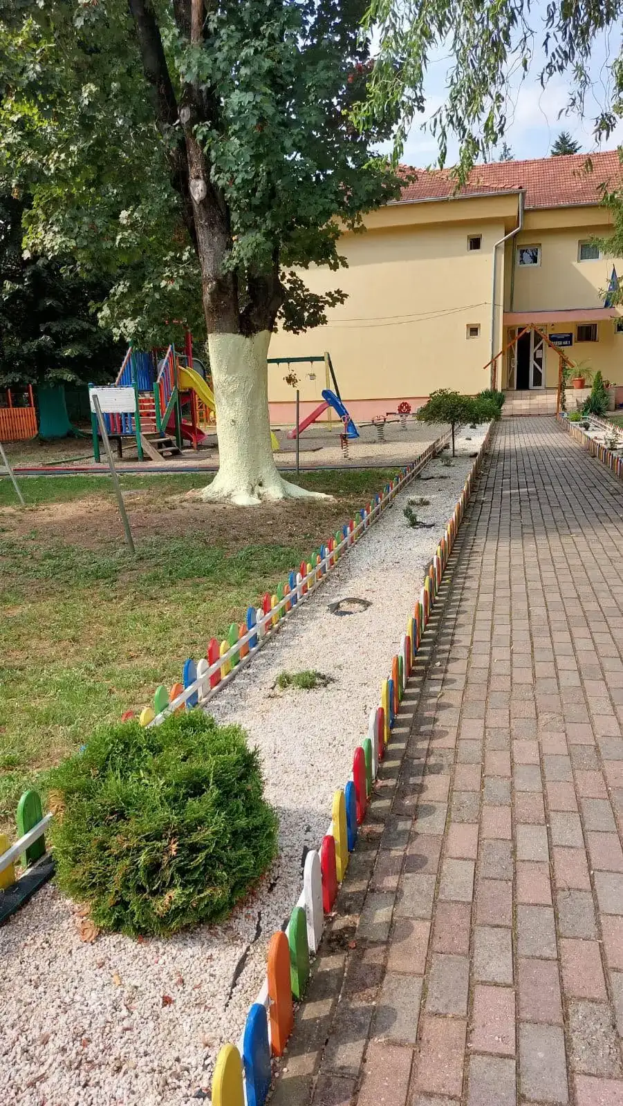 Intrarea în grădiniță, cu gărduleț colorat și loc de joacă în curte