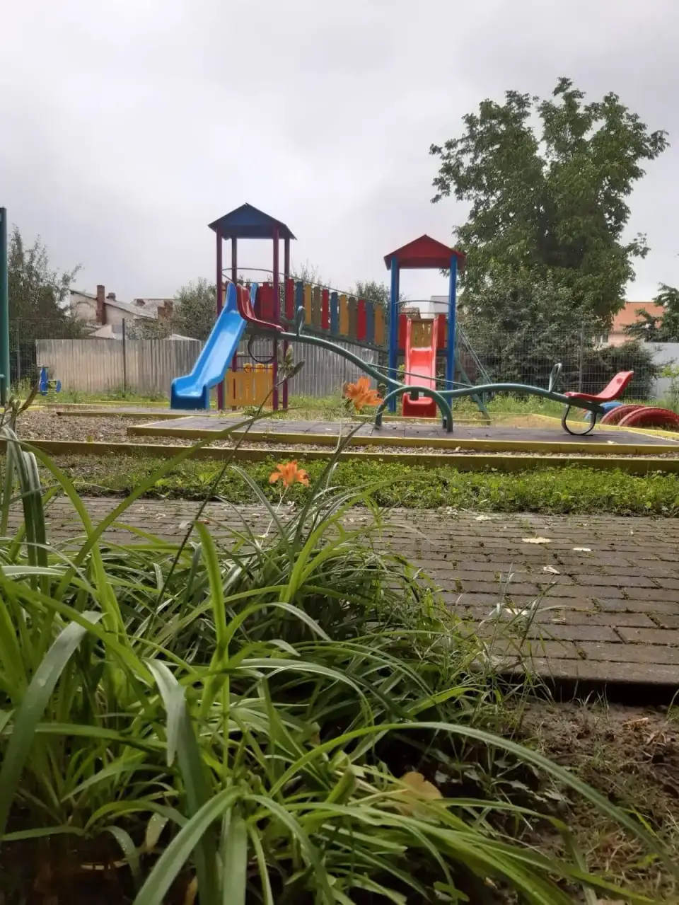 Loc de joacă cu tobogane albastre și roșii, văzut printre flori