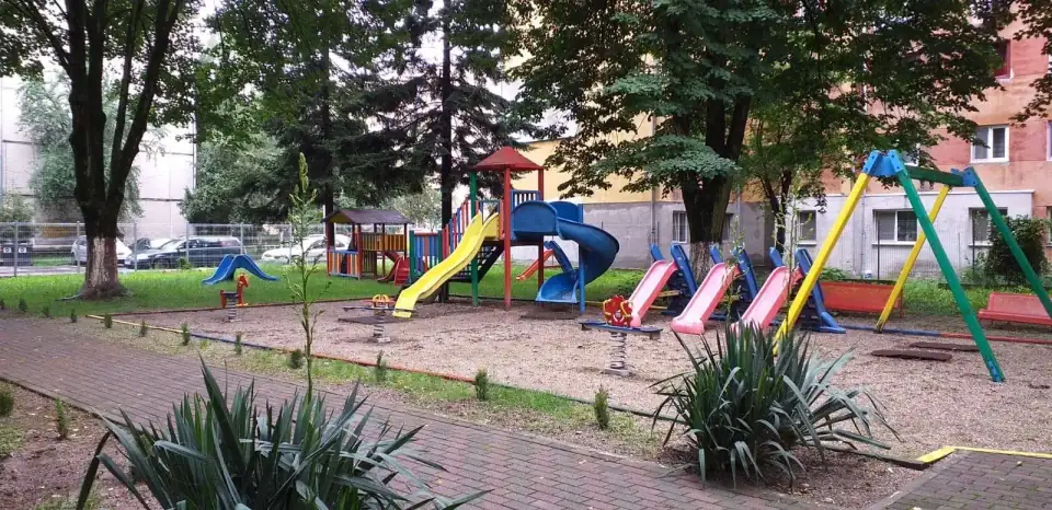 Locul de joacă al grădiniței, cu tobogane, leagăne și căsuțe colorate, la umbra copacilor